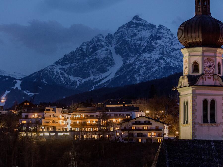 A hotel with multiple floors, a bell tower, and a mountain backdrop.
