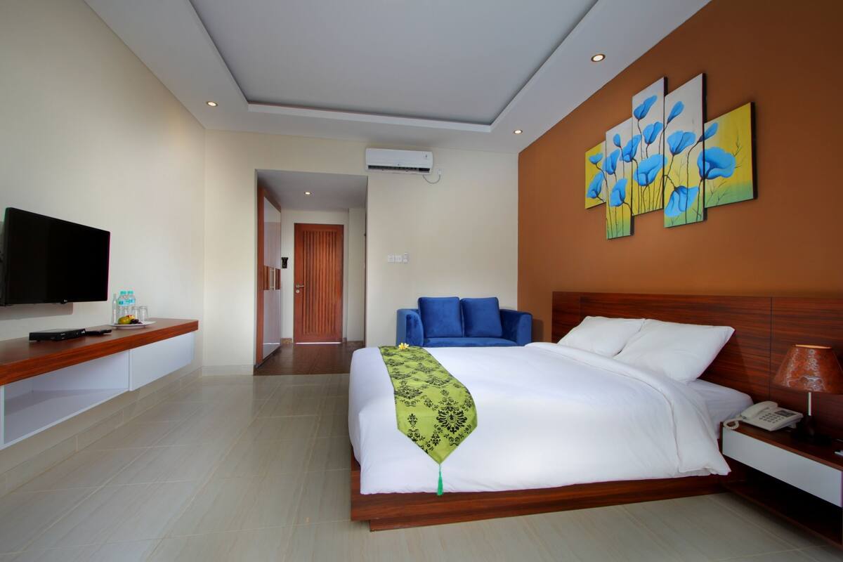 Une chambre d’hôtel moderne dotée d’un grand lit, d’un téléviseur à écran plat, d’une table de chevet avec une lampe et d’un tableau accroché au mur.