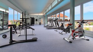 A spacious gym with various exercise equipment, large windows, and a high ceiling. - Umah Bali Suite and Residence (Denpasar)
