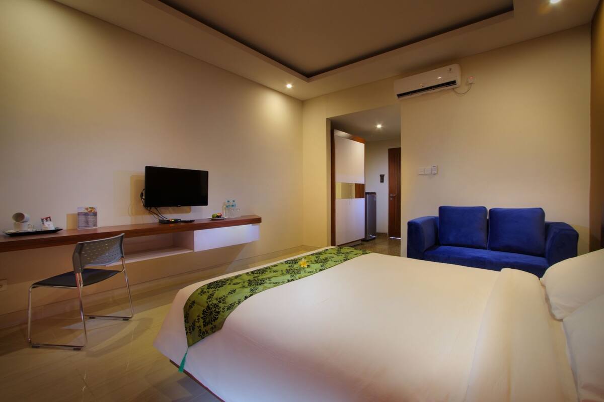 Une chambre d’hôtel avec un lit, un canapé bleu, un bureau avec un téléviseur à écran plat et une chaise.