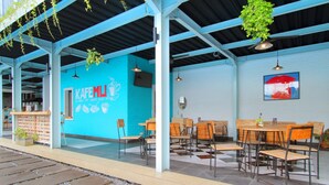 An outdoor cafe with blue walls, wooden tables and chairs, hanging plants, and a red umbrella painting. - Umah Bali Suite and Residence (Denpasar)