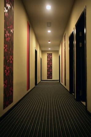 Un pasillo de hotel con alfombra a rayas, puertas a ambos lados y un adorno floral en la pared.