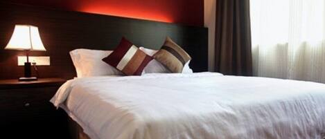A neatly made bed with white linens and two decorative pillows, a bedside lamp, and a dark wooden headboard in a hotel room.
