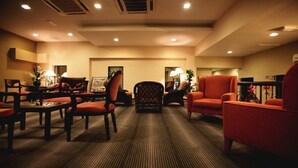 Un hall de hotel con suelo alfombrado, varios sillones, un sofá y una pequeña mesa con una lámpara.