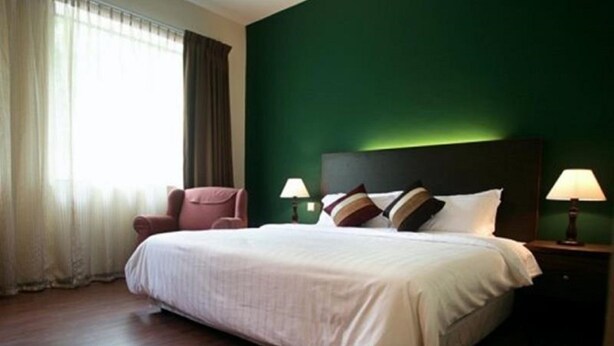 Habitación de hotel con una cama grande, dos lámparas de noche, una silla y una pared verde.