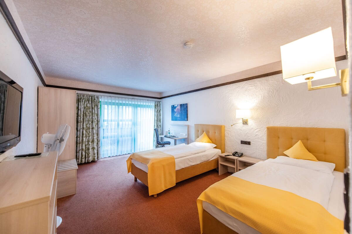 Une chambre d’hôtel avec deux lits, un bureau, une chaise, une télévision et une fenêtre avec des rideaux.