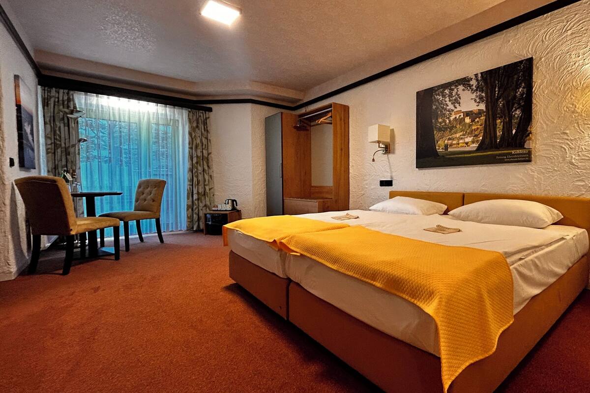 Una habitación de hotel con cama, una silla, una mesa, un espejo y una lámpara adosada a la pared.