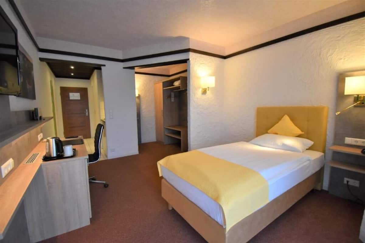 Habitación de hotel con cama, escritorio, silla y televisor montado en la pared.