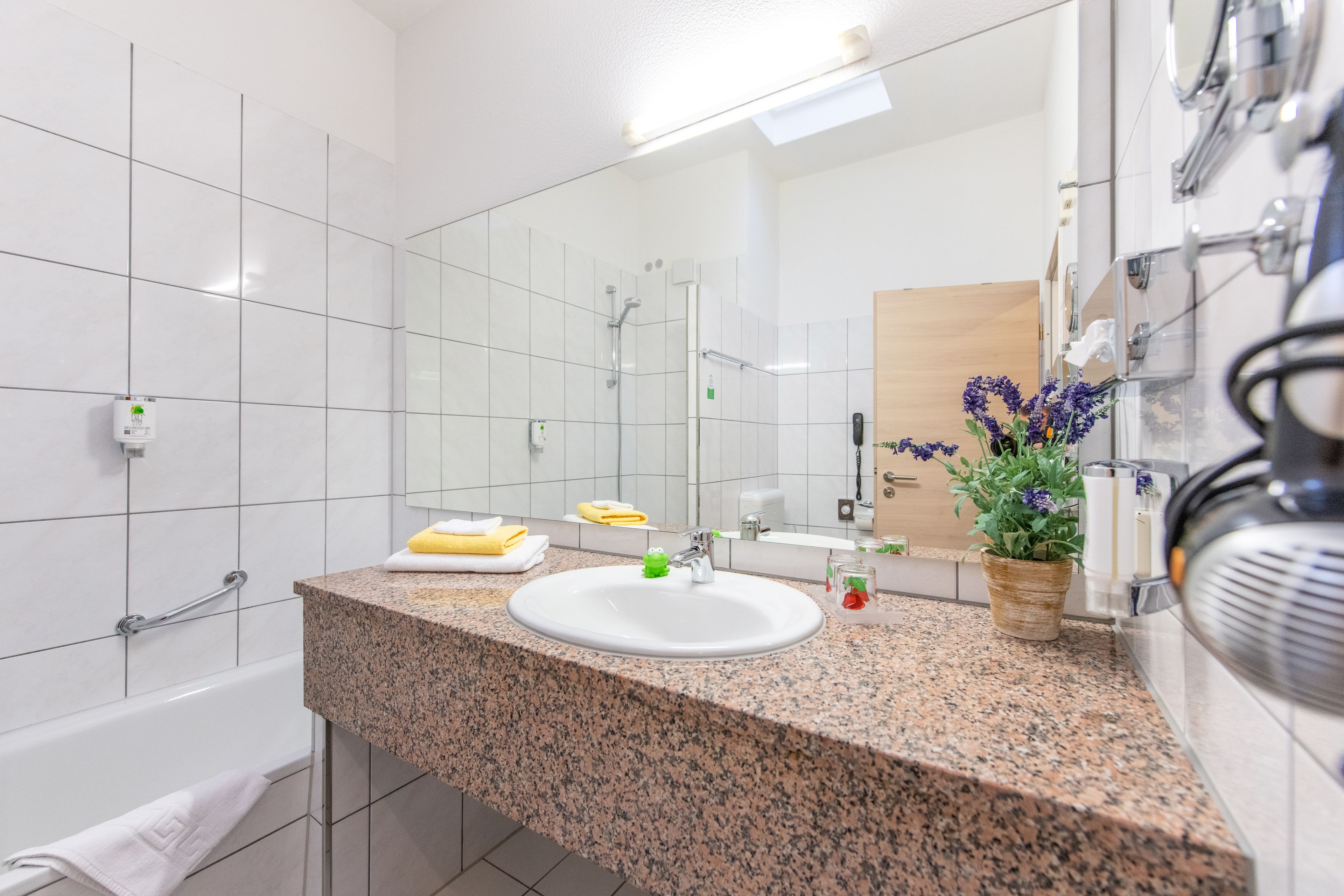 A modern bathroom with a granite countertop, white sink, and a large mirror.