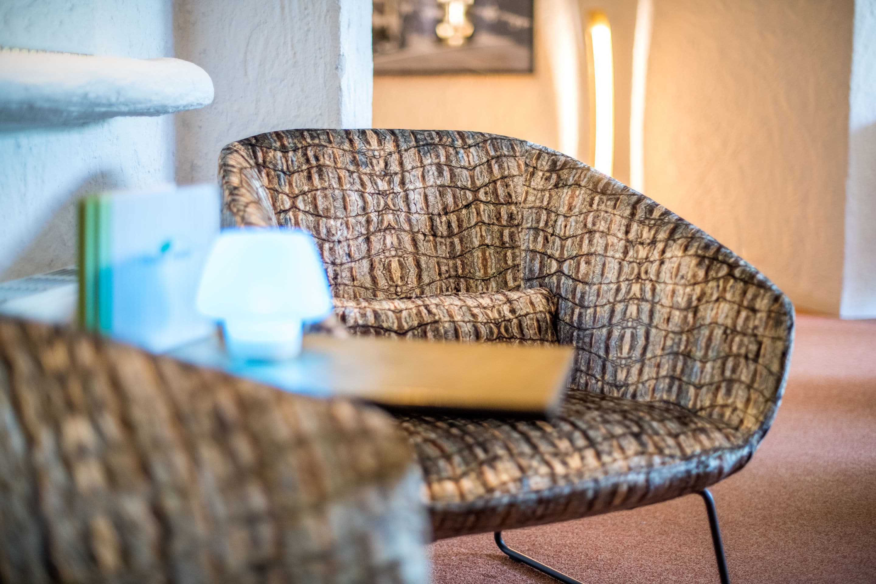 A textured armchair with a cushion, a small table with a book, and a framed picture on the wall.