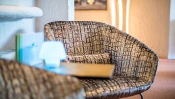 A textured armchair with a cushion, a small table with a book, and a framed picture on the wall.