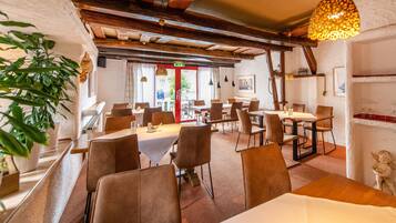 Un restaurante con vigas de madera, paredes blancas y una puerta roja. Mesas y sillas dispuestas para comer.