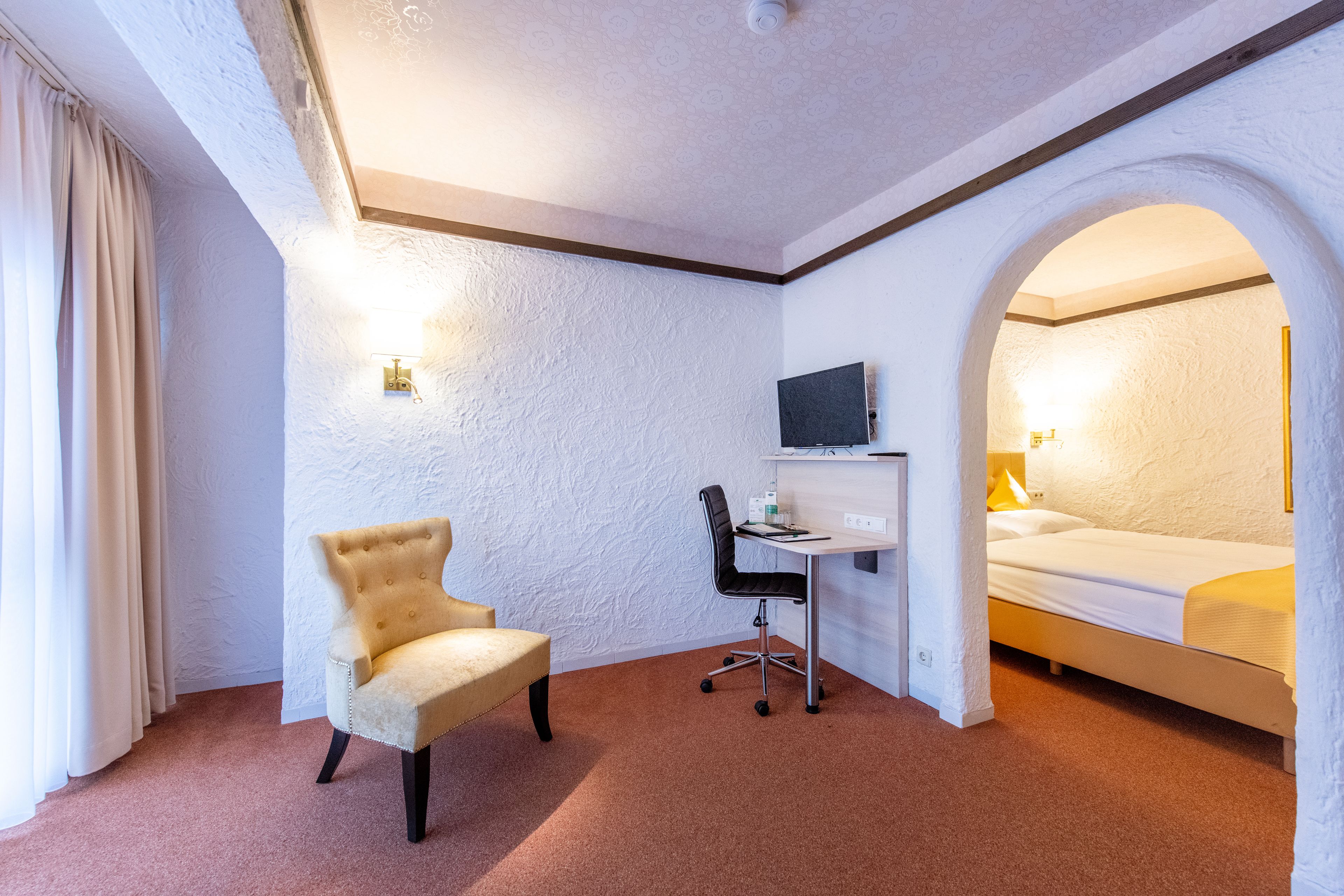 A hotel room with a bed, a desk with a computer, a chair, and a television.