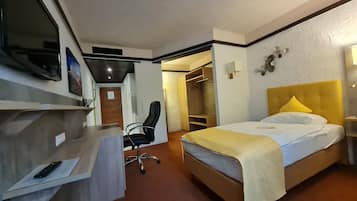 A hotel room with a bed, desk, chair, wardrobe, and a television.