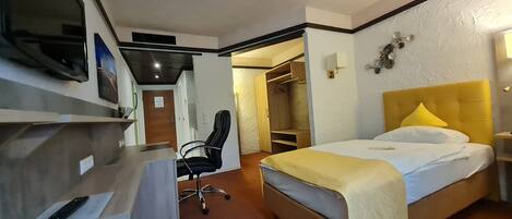 A hotel room with a bed, desk, chair, wardrobe, and a television.
