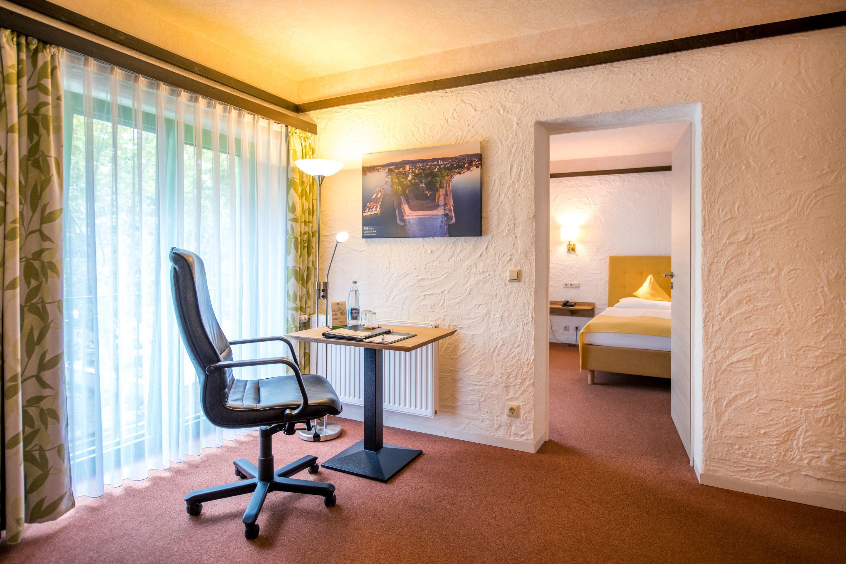 Een hotelkamer met een bureau, stoel, bed en een schilderij aan de muur.