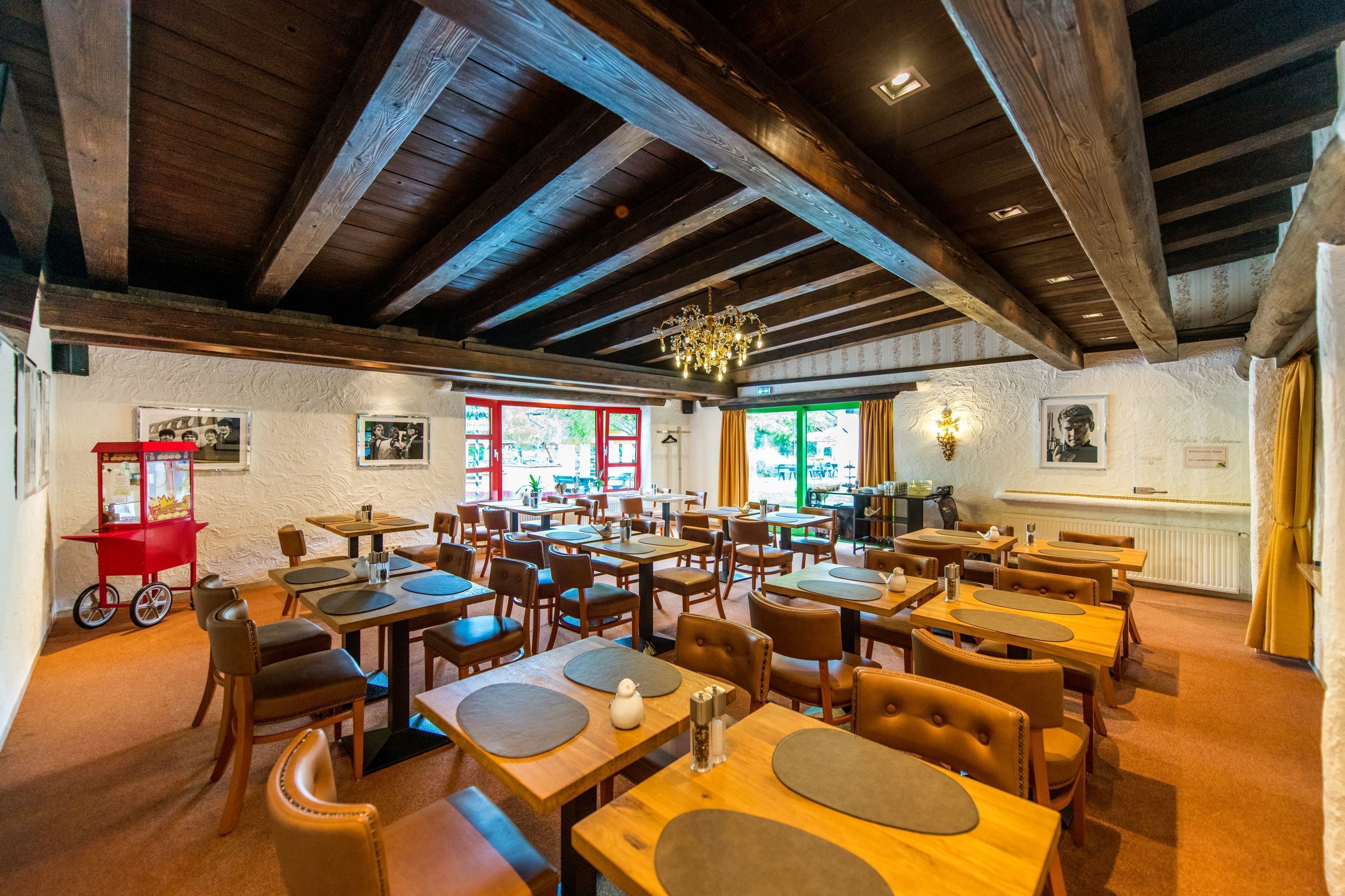 Un restaurante con mesas y sillas de madera, una araña y cuadros en las paredes.