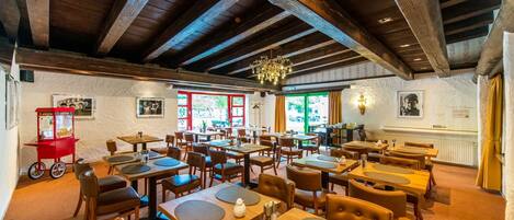 A restaurant with wooden tables and chairs, a chandelier, and framed pictures on the walls.