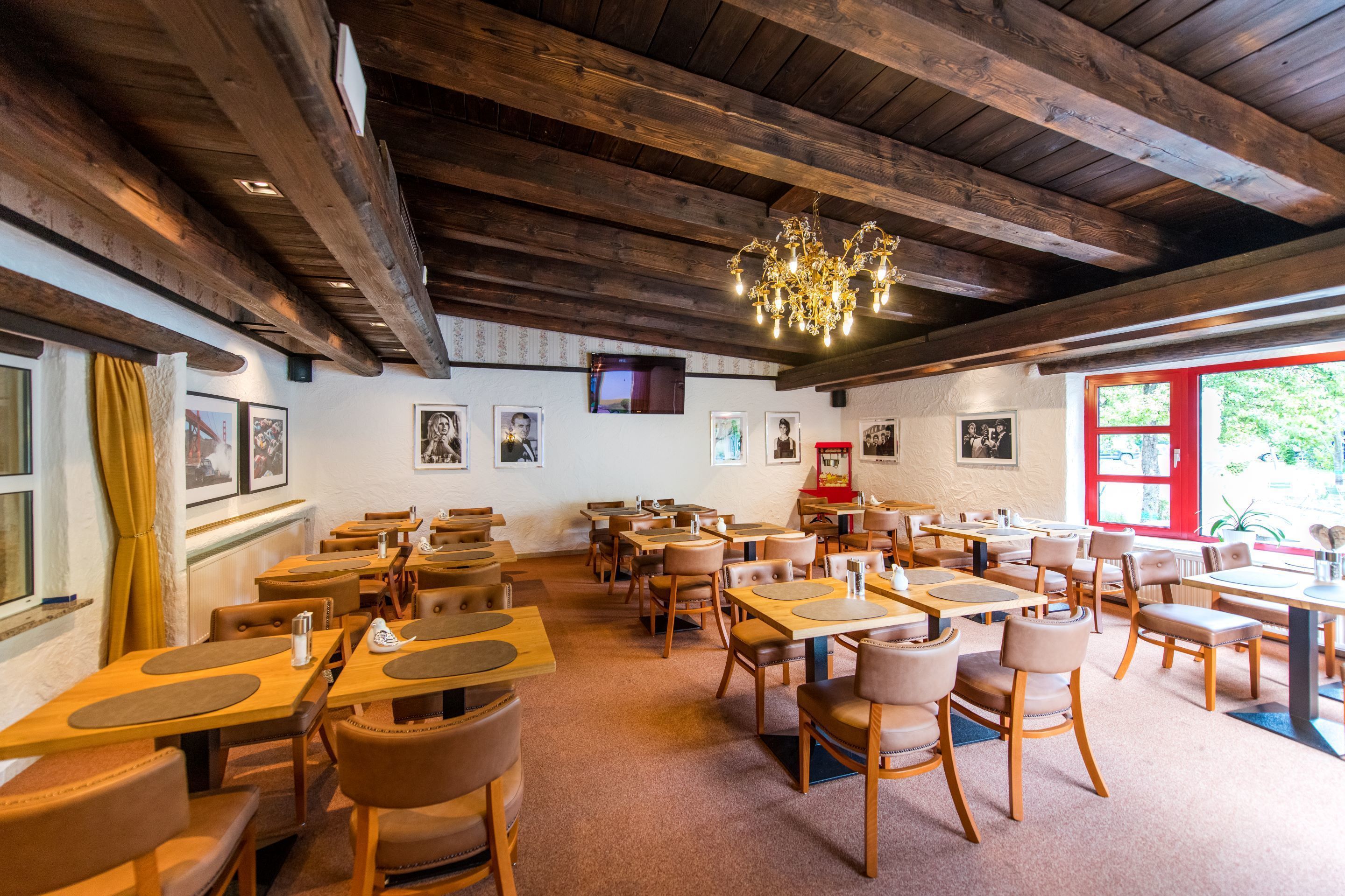 A restaurant with wooden tables and chairs, a chandelier, and framed pictures on the walls.