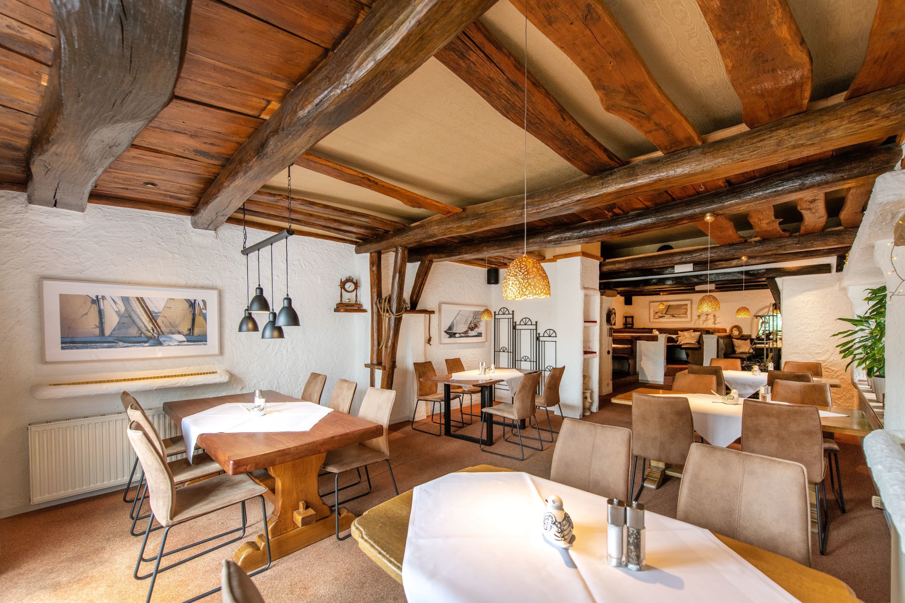 Un restaurante con vigas de madera, paredes blancas y una variedad de mesas dispuestas.