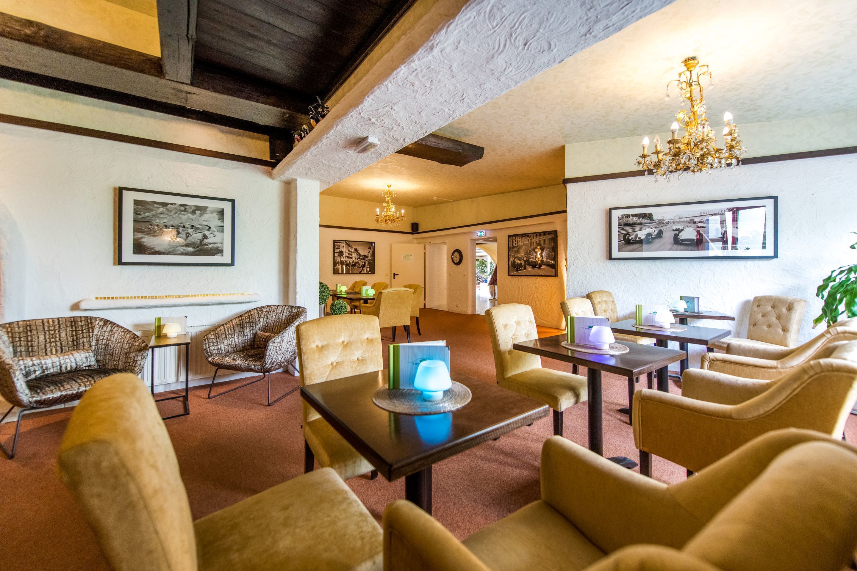 Um hall de hotel com uma mistura de mobiliário moderno e clássico, incluindo sofás e poltronas, uma mesa de centro com abajur, e quadros nas paredes.