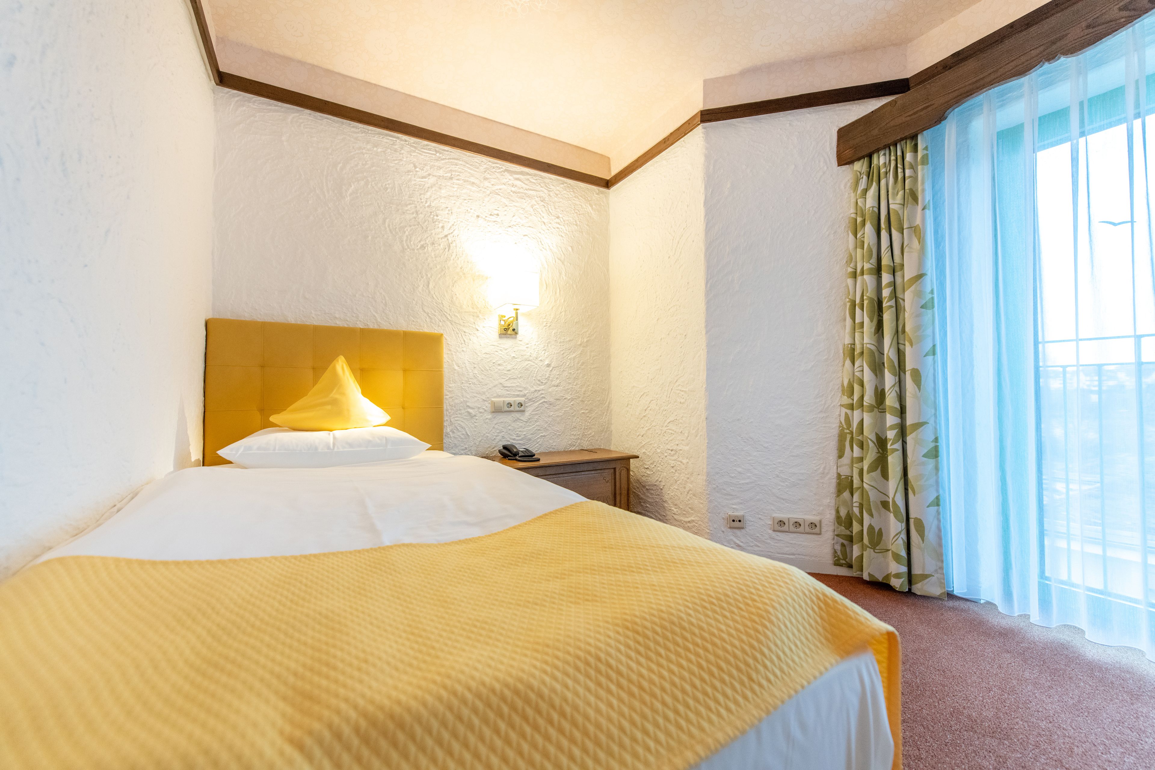 A hotel room with a large bed, a bedside table, a lamp, and a window with curtains.