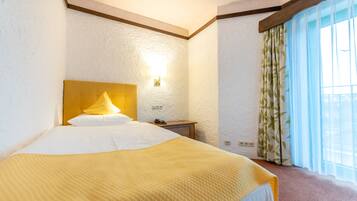 A hotel room with a large bed, a bedside table, a lamp, and a window with curtains.