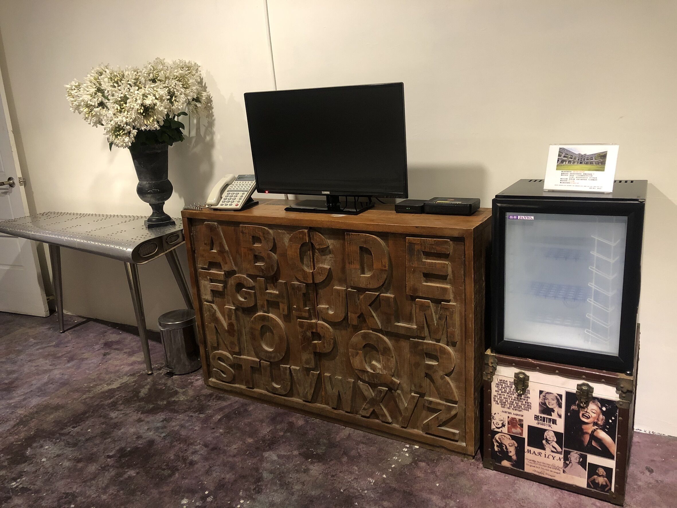 A reception desk with a computer monitor, a telephone, and a small refrigerator.