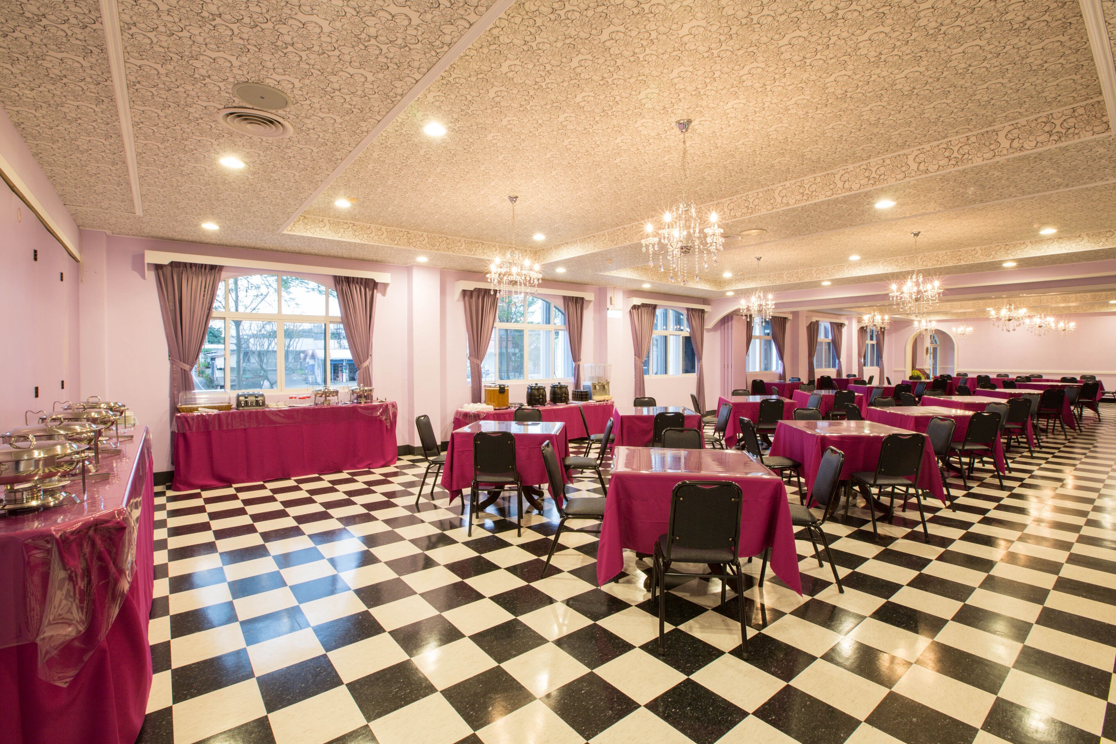 Un salón de banquetes con suelo a cuadros, mesas con manteles rosas y candelabros.