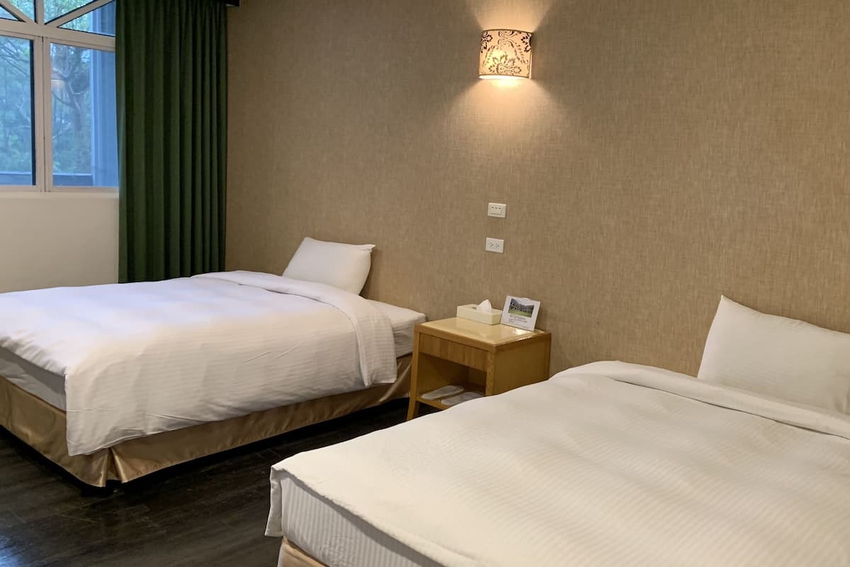 Ein Hotelzimmer mit zwei Betten, einem Nachttisch mit Lampe und einem Fenster mit Vorhängen.