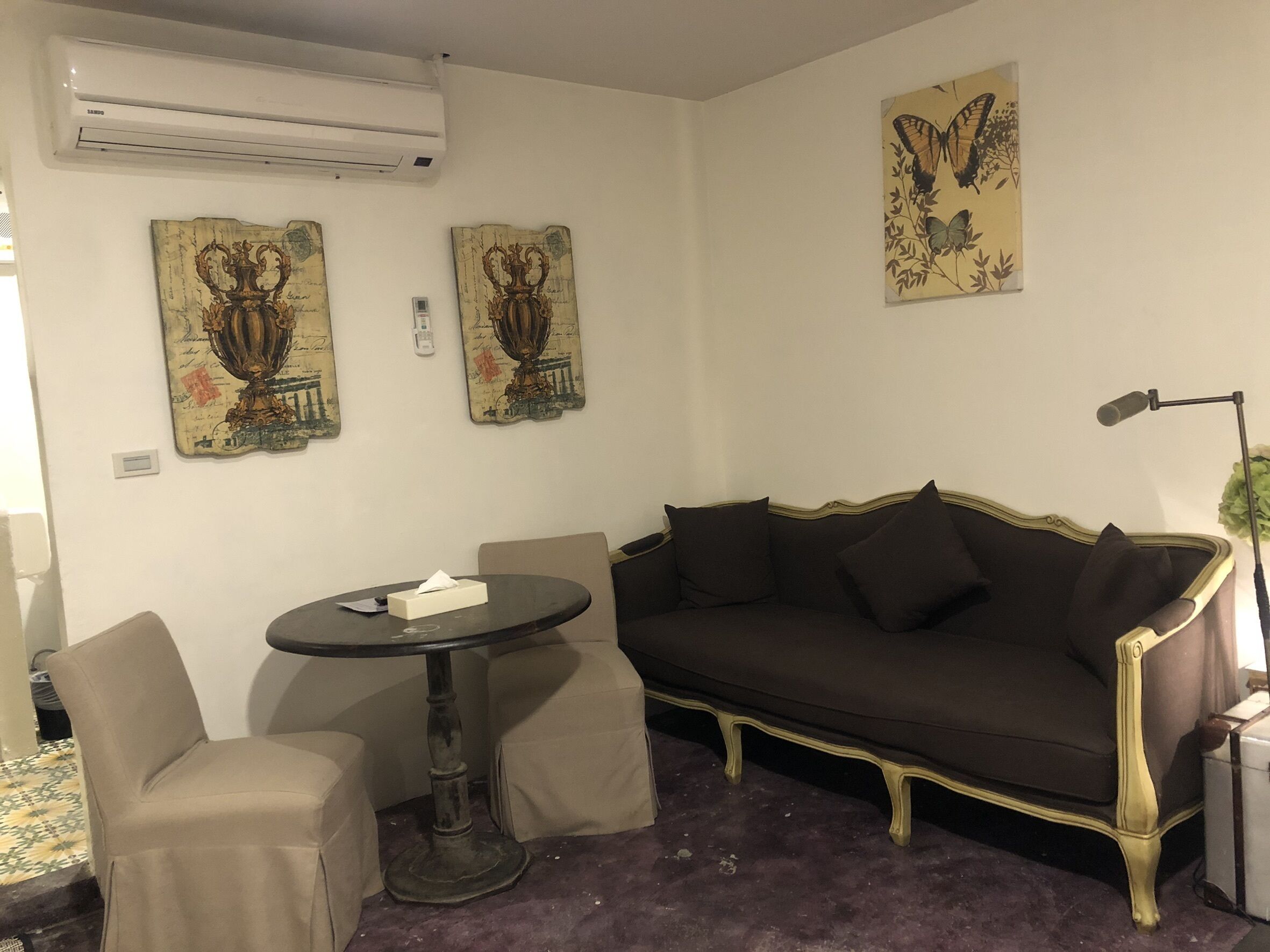 A room with a dark brown sofa, two beige armchairs, a small round table with a tissue box, and two wall-mounted decorative pieces.