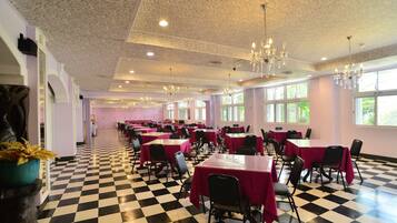 A banquet hall with checkered flooring, tables with red tablecloths, and chandeliers.