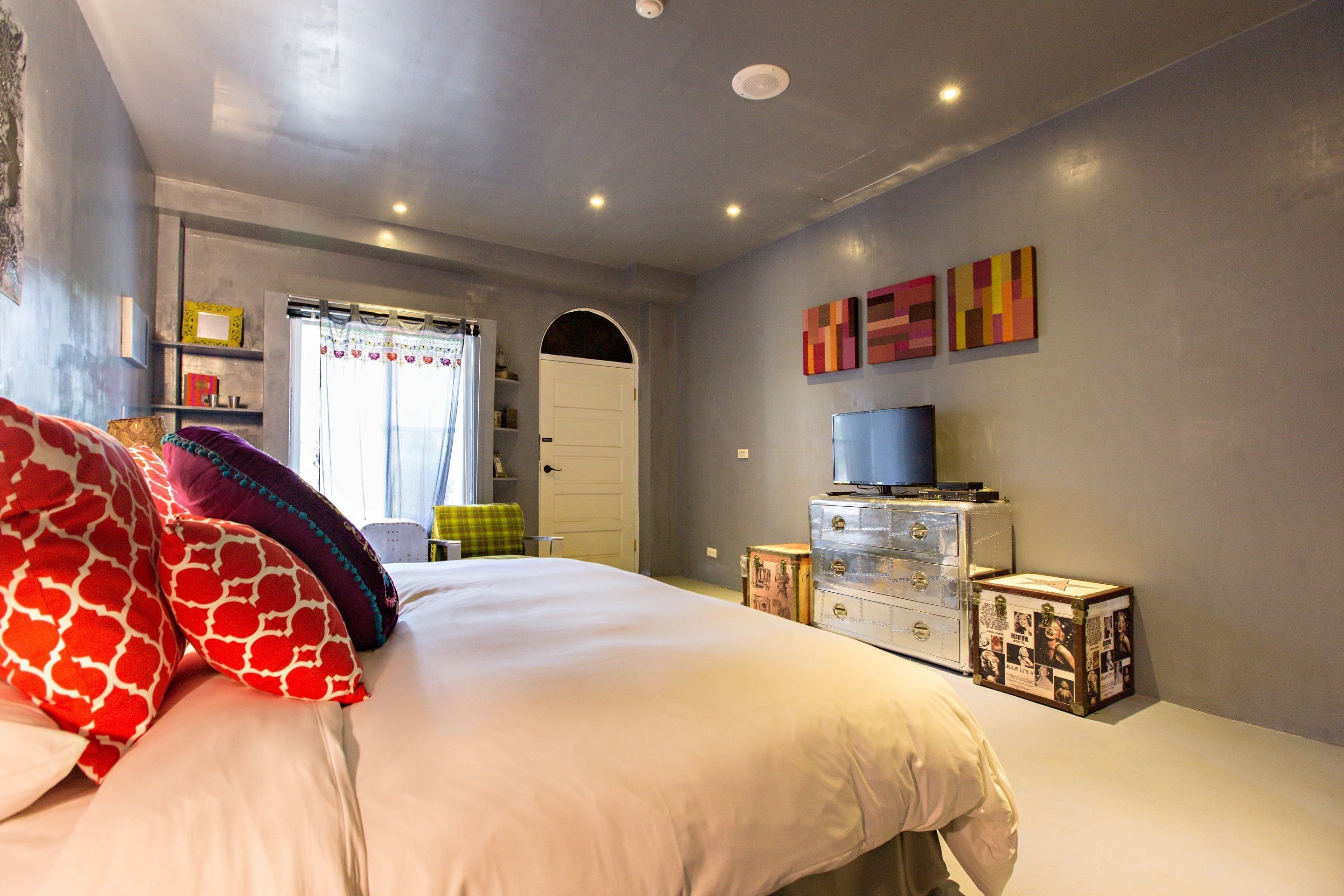 A bedroom with a bed, a dresser, a television, and a door.