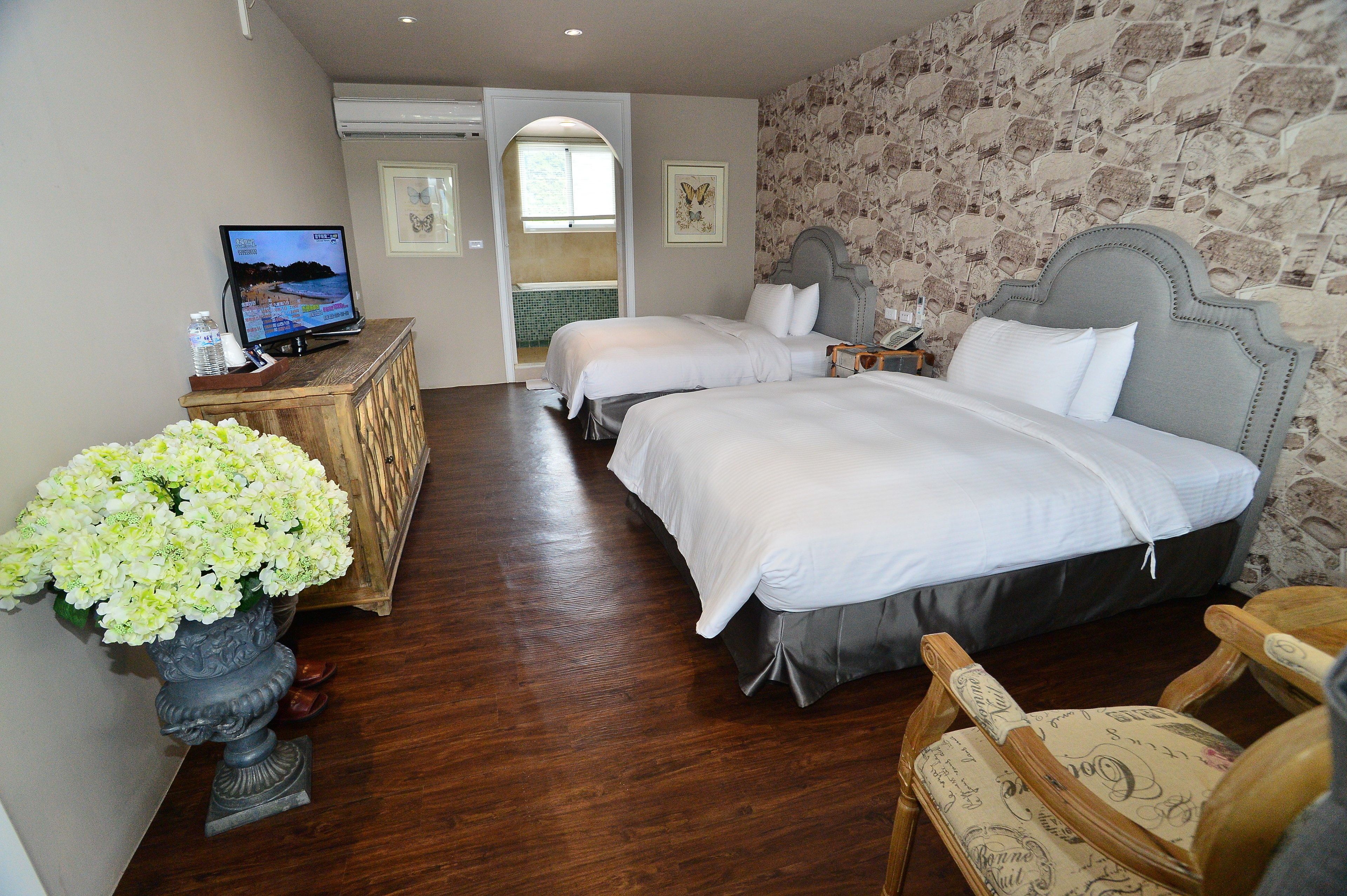 A hotel room with two beds, a television, a wooden dresser, and a vase of flowers.