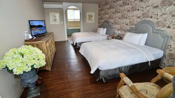 A hotel room with two beds, a television, a wooden dresser, and a vase of flowers.