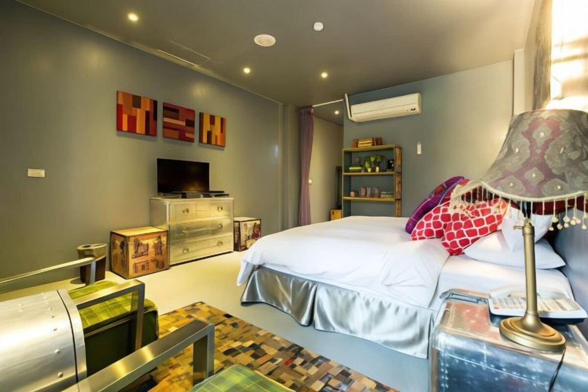 A bedroom with a bed, bedside table, lamp, dresser, TV, and decorative pillows.