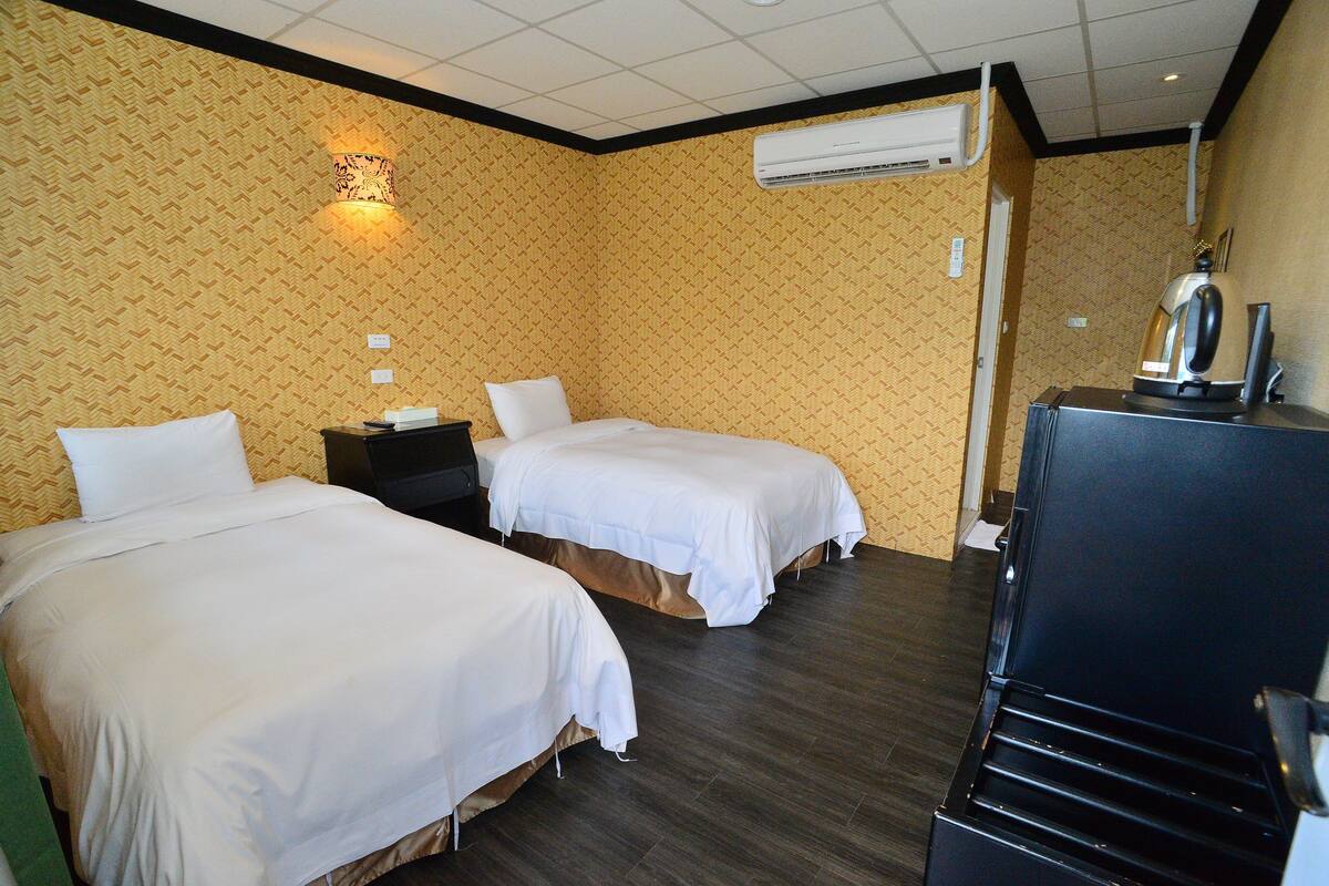 Ein Hotelzimmer mit zwei Betten, einem Nachttisch, einer Klimaanlage und einem Wasserkocher.