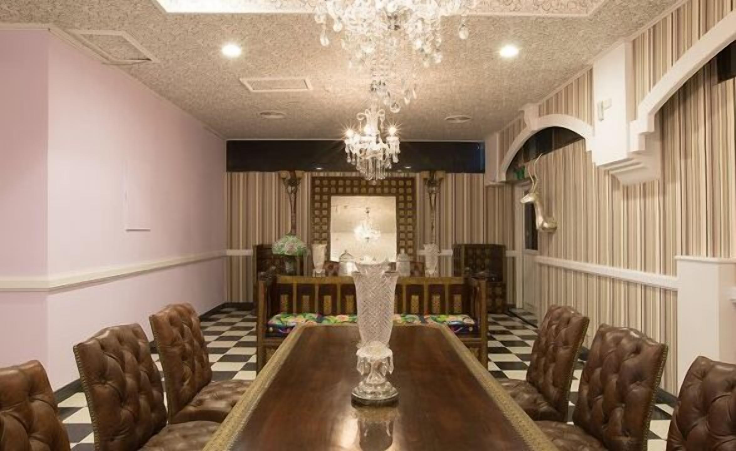 Un comedor formal con una larga mesa, sillas de cuero, una araña y un papel tapiz estampado.