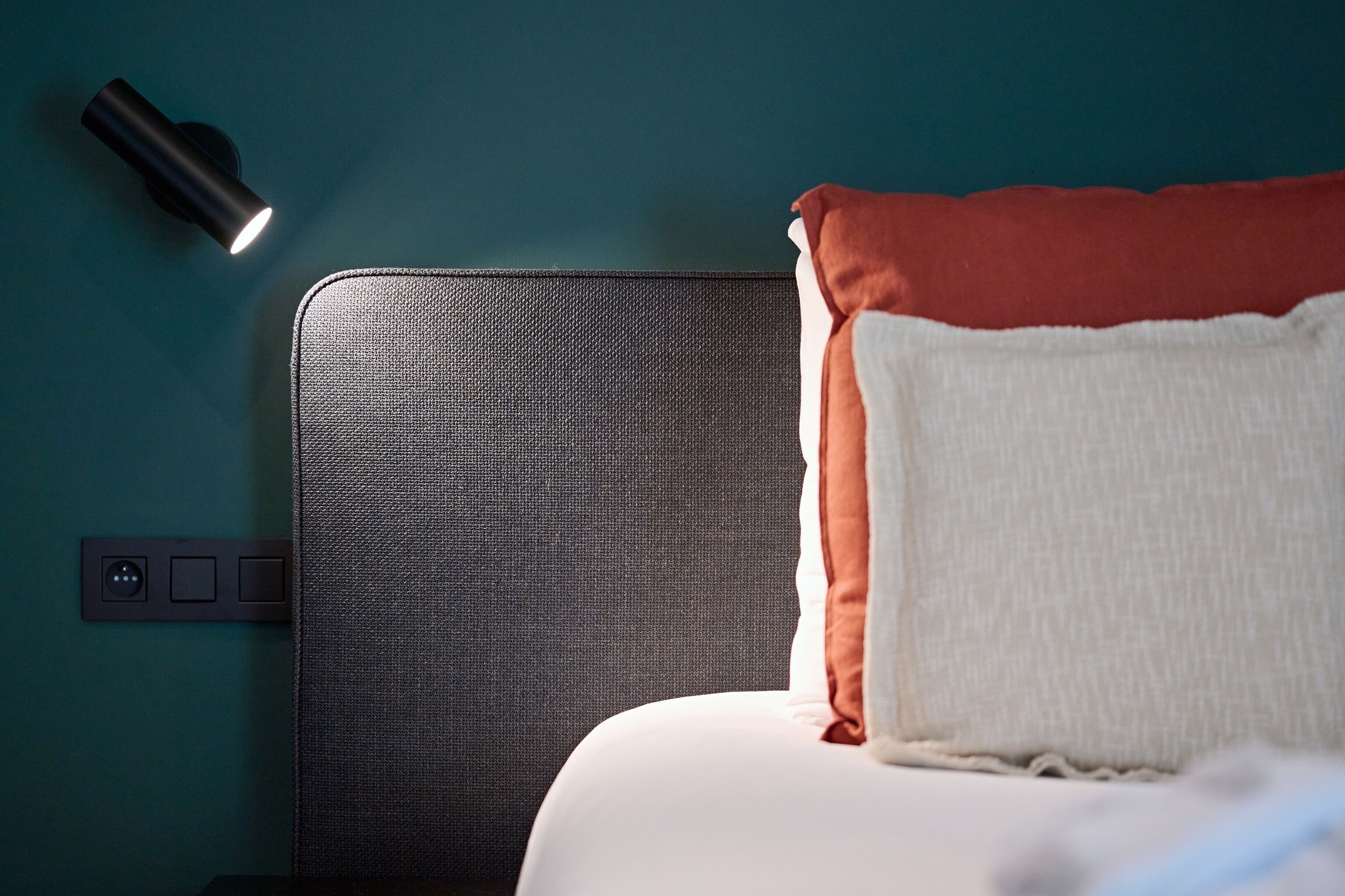 Un lit avec une tête de lit à motifs, une lampe de chevet et une prise électrique sur le mur.