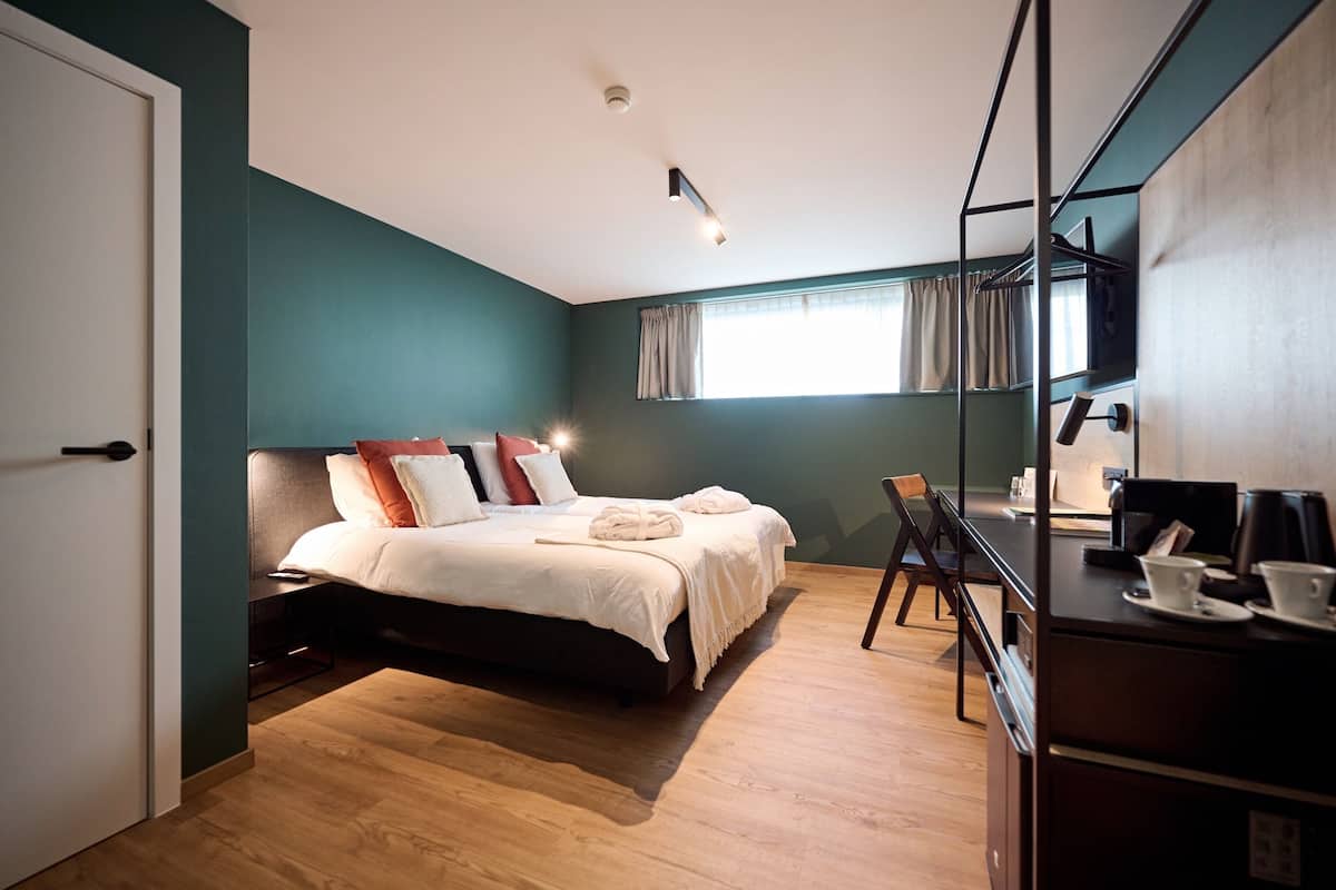 A modern hotel room with a bed, a desk, and a coffee machine.