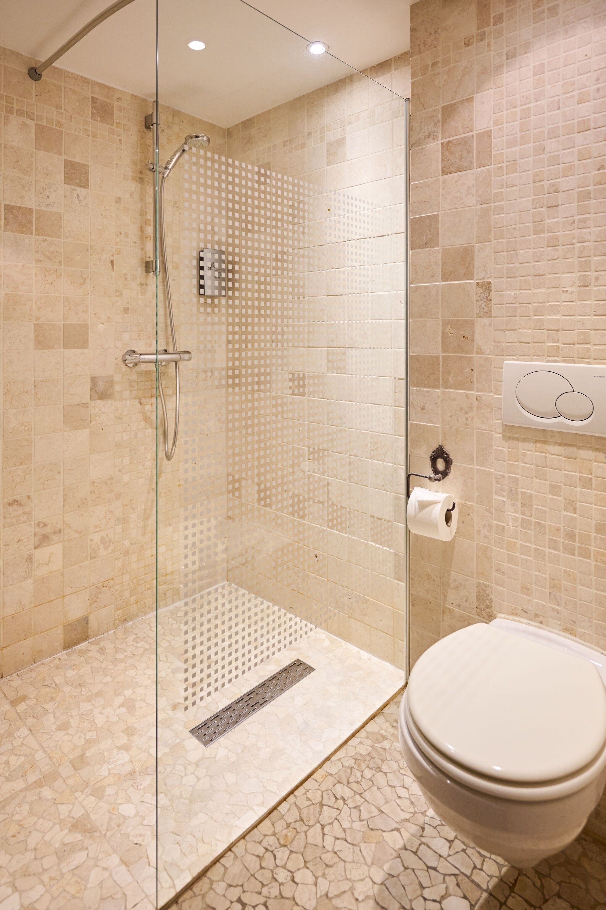 Un baño con ducha de vidrio, inodoro y dispensador de papel higiénico en la pared.