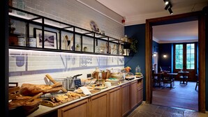 A well-lit kitchen with a long counter, various food items, and a brick wall with shelves above. - Hotel la Malle Poste (Rochefort)