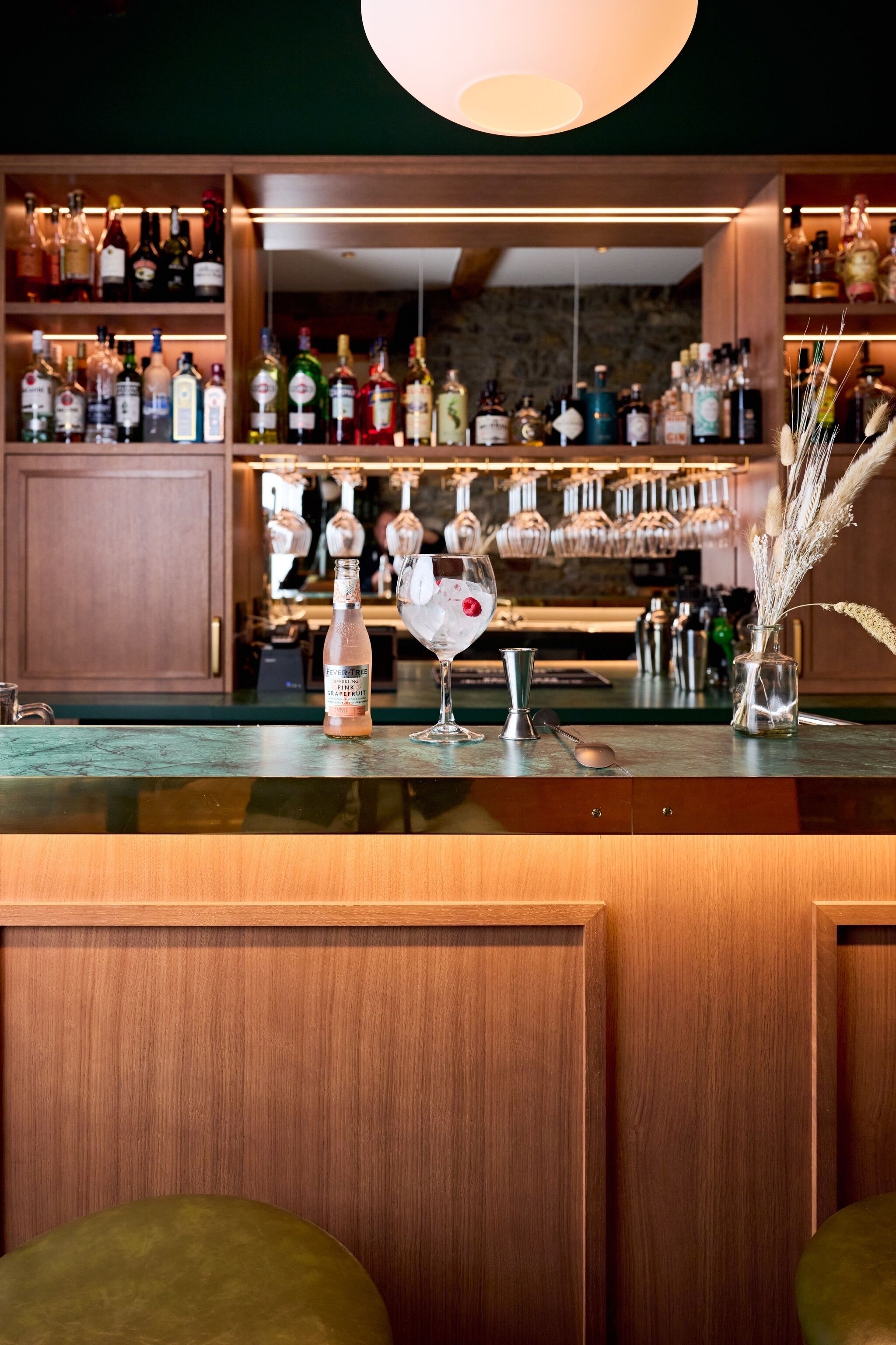 A bar area with shelves of liquor bottles, a bottle of whiskey, a glass, and a spoon on the counter.