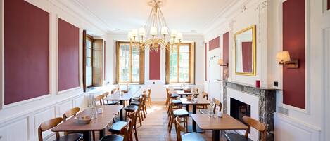 Un comedor elegante con mesas y sillas de madera, un candelabro y ventanas amplias.