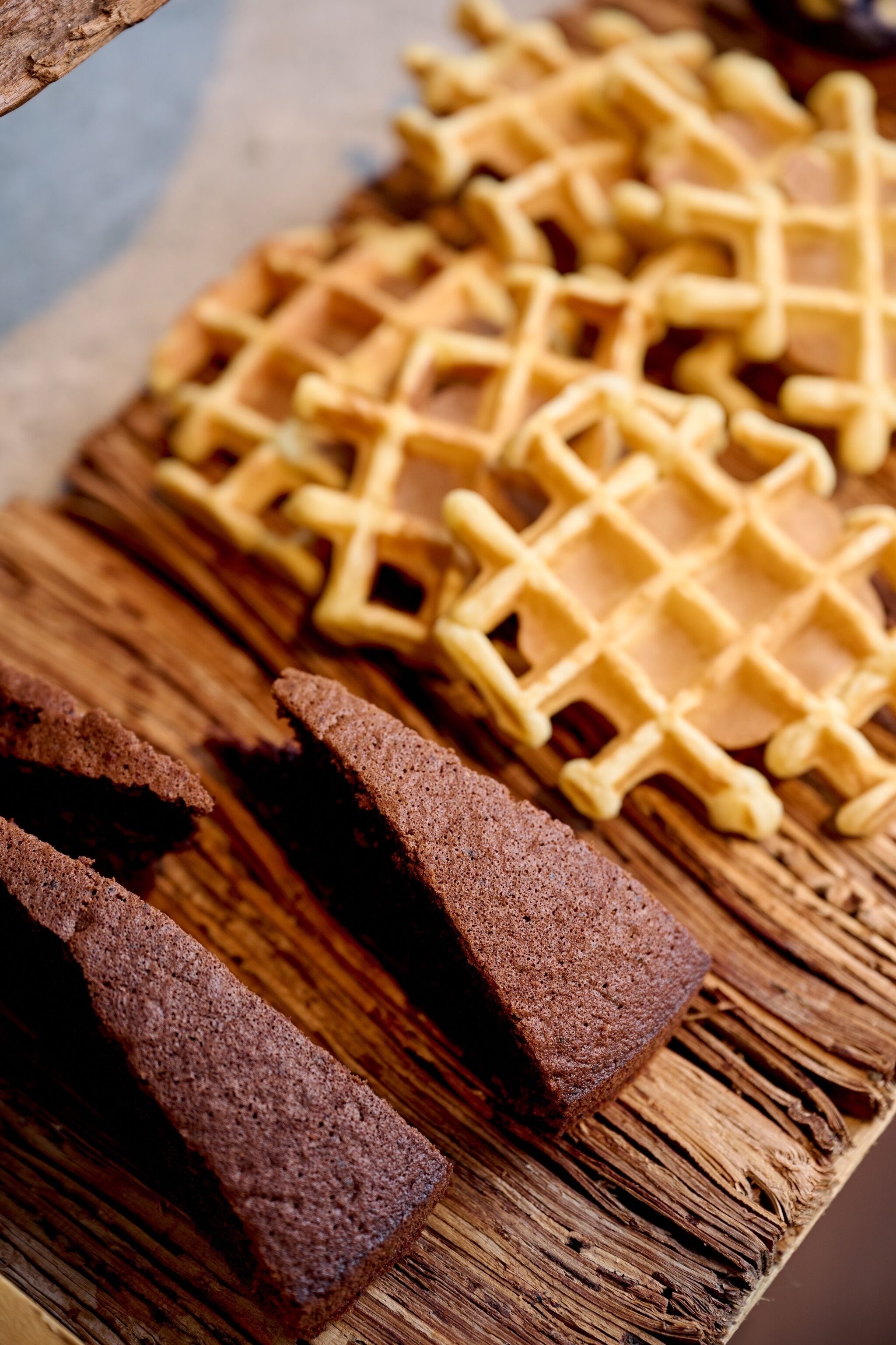 A wooden cutting board with waffles and slices of brown bread.