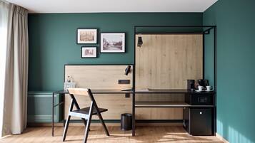 A room with a desk, chair, and a wardrobe. There are framed pictures on the wall.