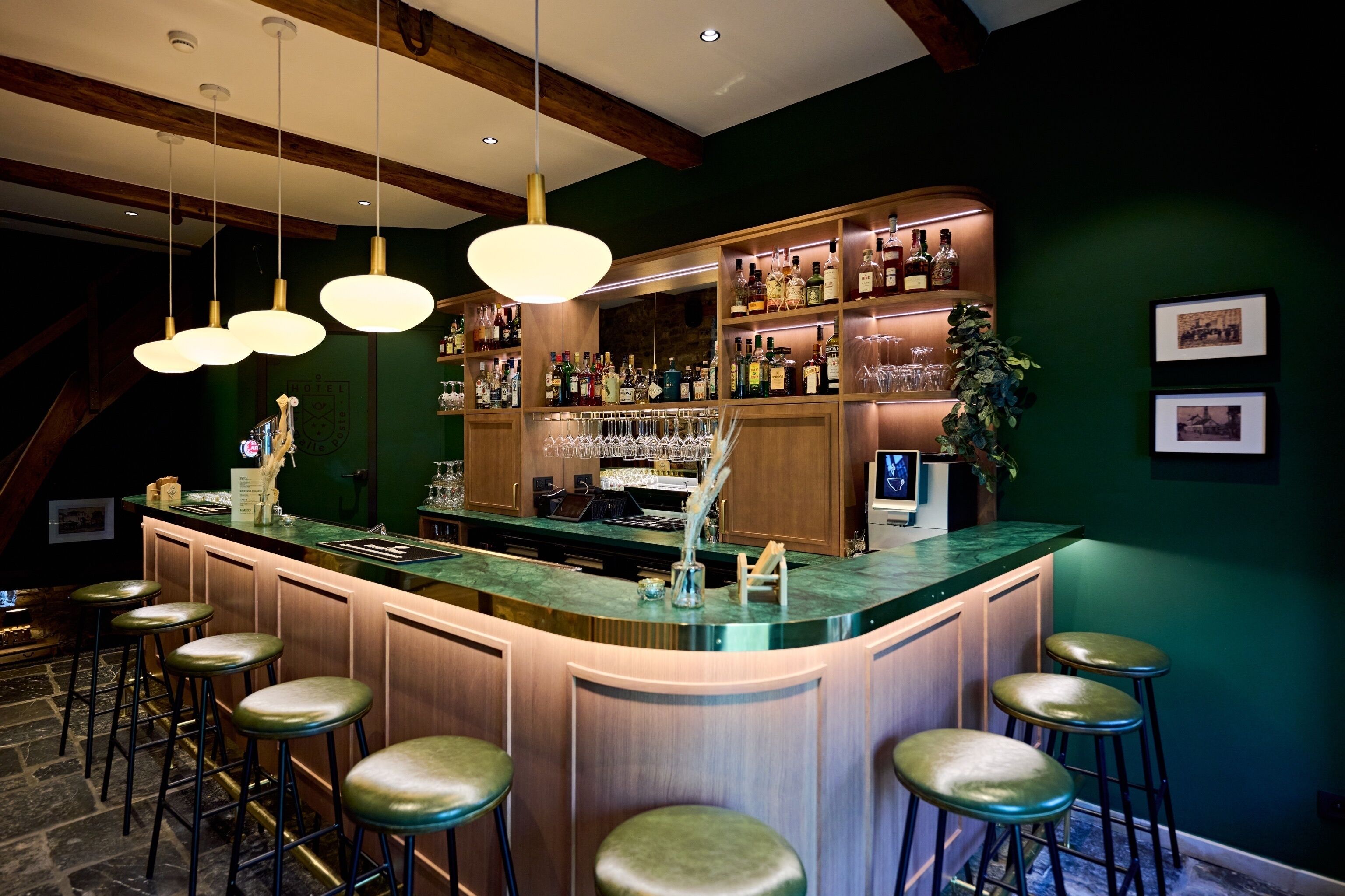 A bar area with a curved counter, multiple stools, hanging pendant lights, and shelves stocked with bottles and glasses.