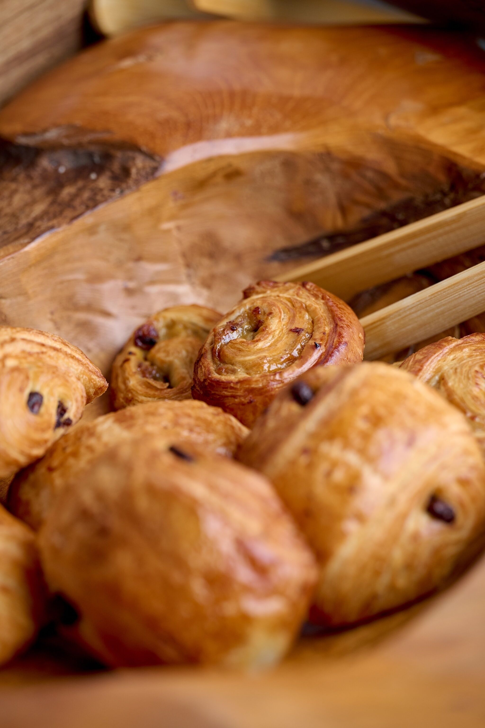 A variety of pastries, including croissants and chocolate-filled pastries, displayed in a wooden basket.