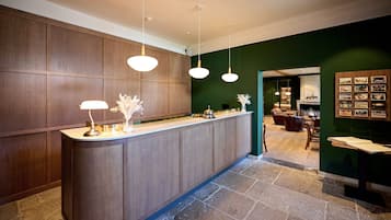 Una zona de recepción con mostrador de madera, iluminación colgante y una pared verde con cuadros enmarcados.