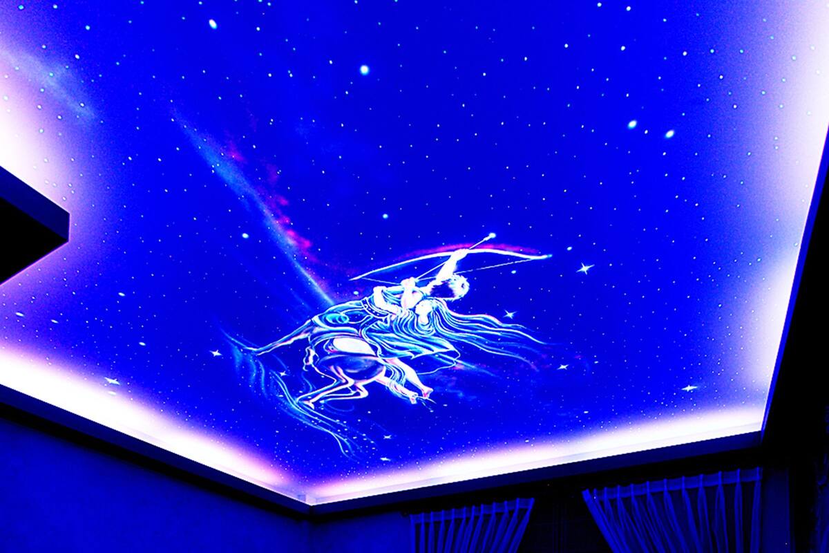 A room with a starry ceiling projection, two beds, and a television on the wall.